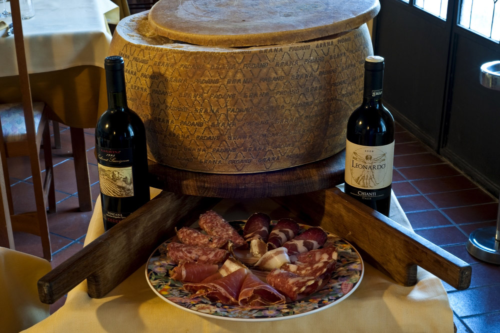 Piatto di salumi toscani davanti a una forma di formaggio e a due bottiglie di Chianti